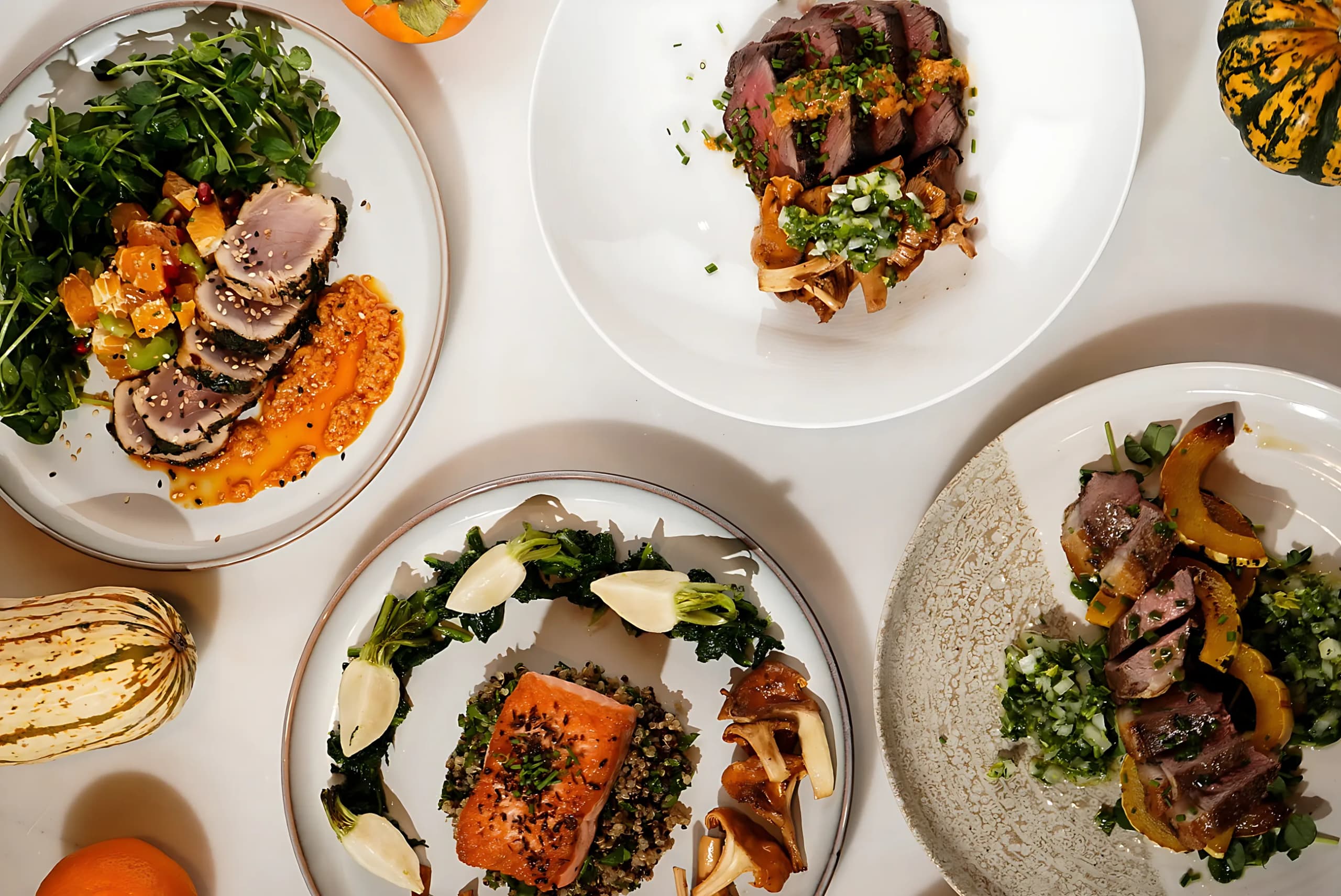 A table set with several plates of salmon, duck and roasted vegetables