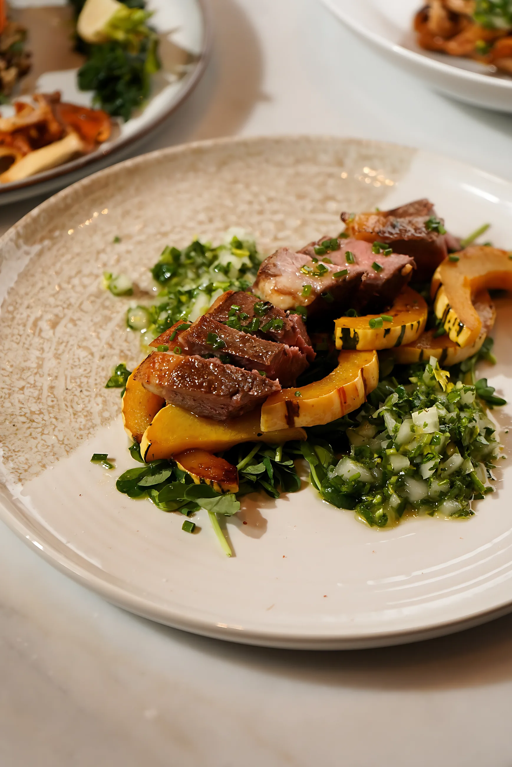 Seared duck breast over greens with roasted squash on a stoneware plate