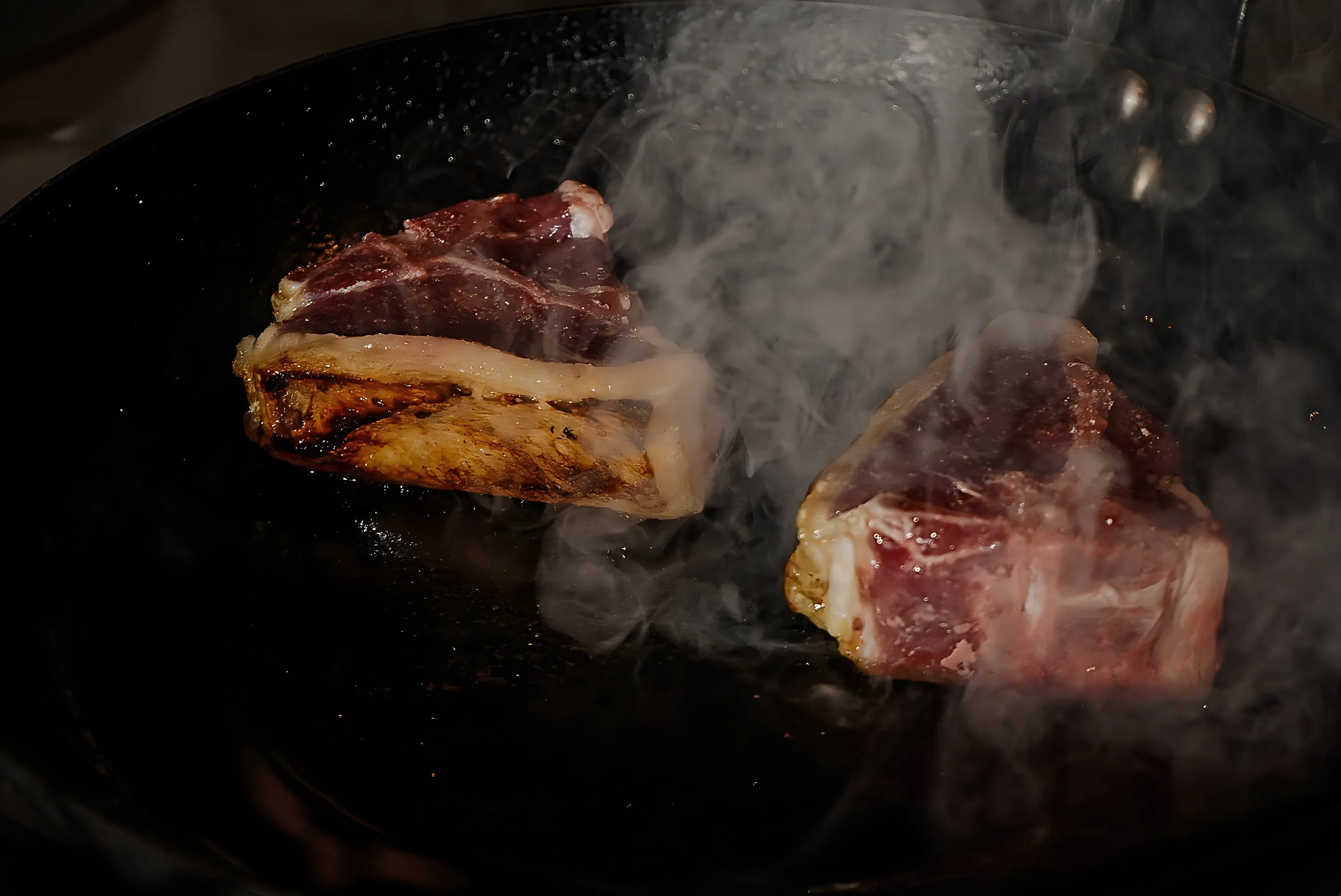 Lamb chops searing in a cast iron pan with smoke rising