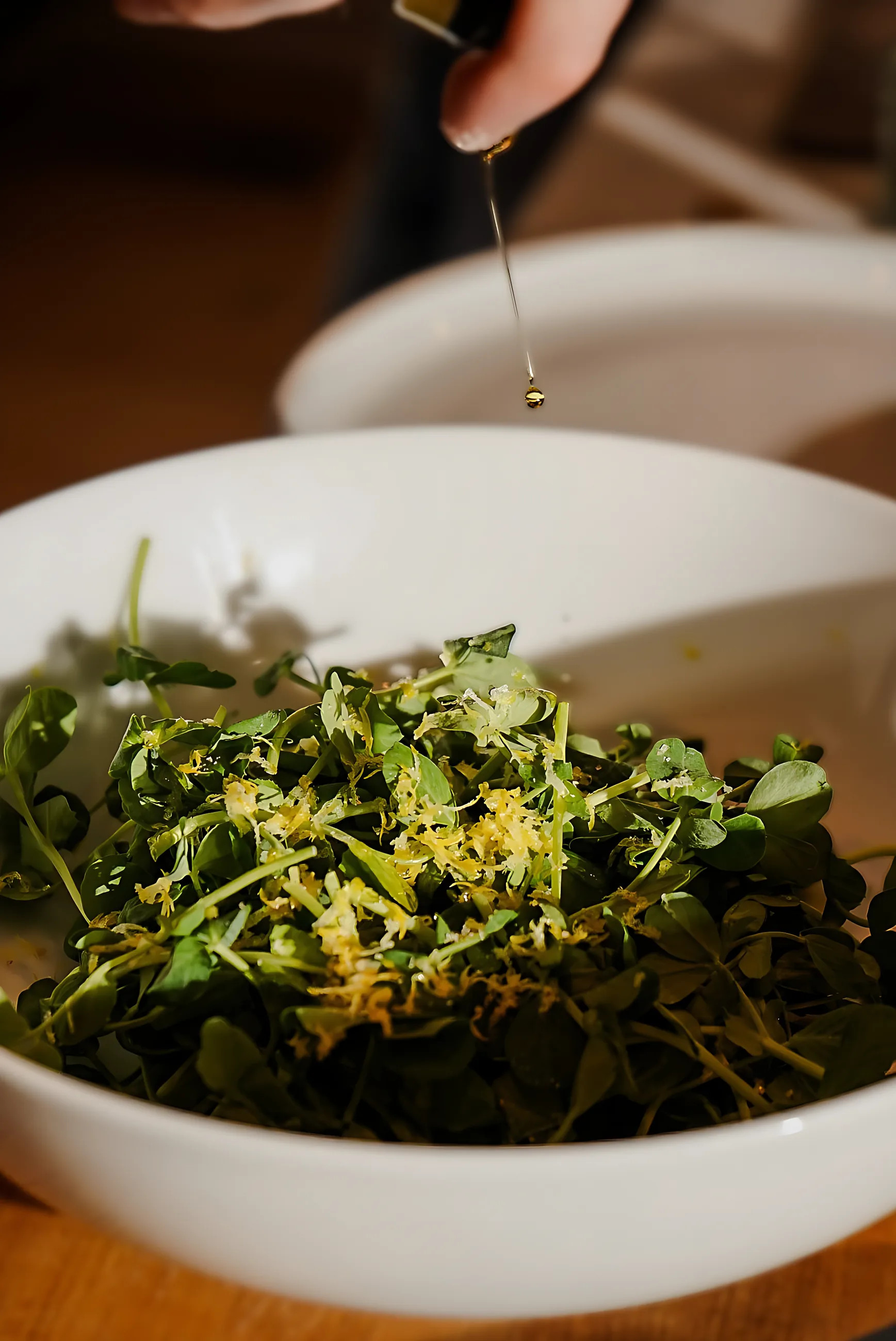 Olive oil drizzled over a bowl of greens with lemon zest