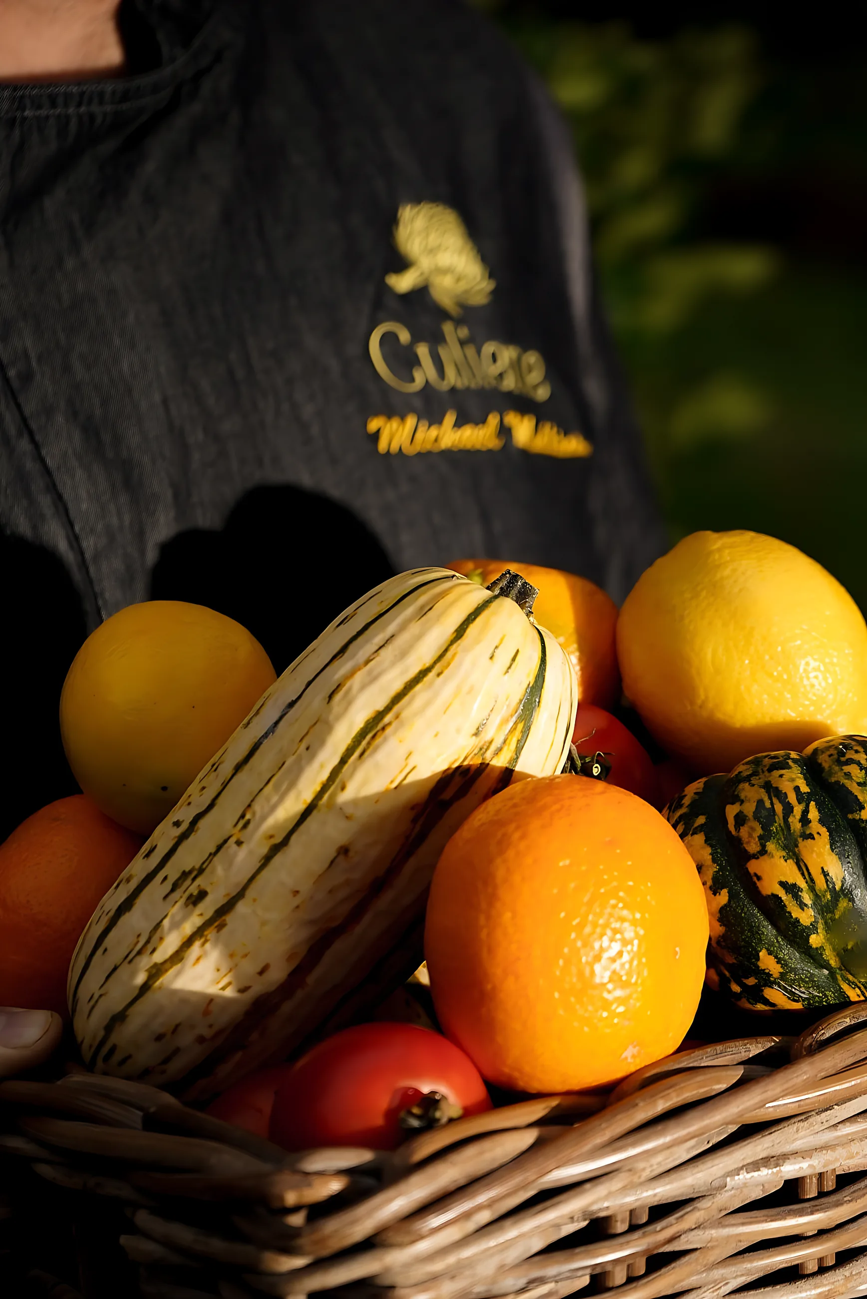 A basket of winter squash, persimmons, citrus and plums held by a chef
